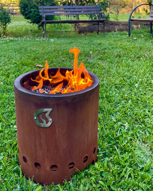 Humos Brasero sin Humo metal fire pit burning with bright flames on grassy lawn for camping