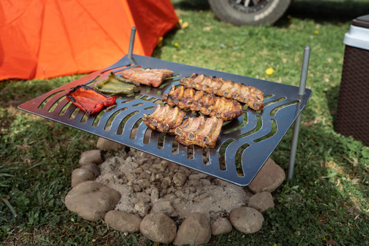 Humos Parrilla Camping grill with ribs and peppers cooking over a stone fire pit outdoors