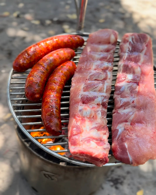 Parrilla inoxidable Humos para camping con salchichas y costillas cocinándose al aire libre