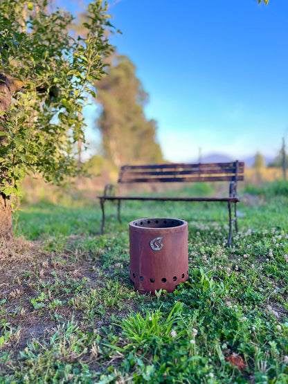 Humos Brasero sin Humo portable camping fire pit on grass with a bench in the background