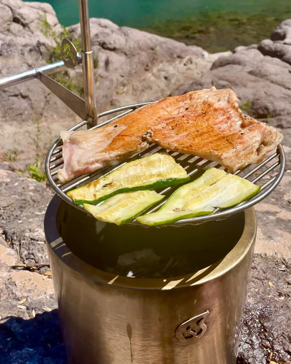 Parrilla Inoxidable Humos para camping con carne y verduras asándose sobre fuego al aire libre